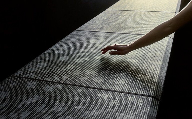 A hand reaching toward a textured, illuminated surface with a dark background and warm lighting.