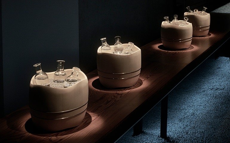 Three wooden containers with glass bottles inside, illuminated by soft lighting on a dark wooden surface.