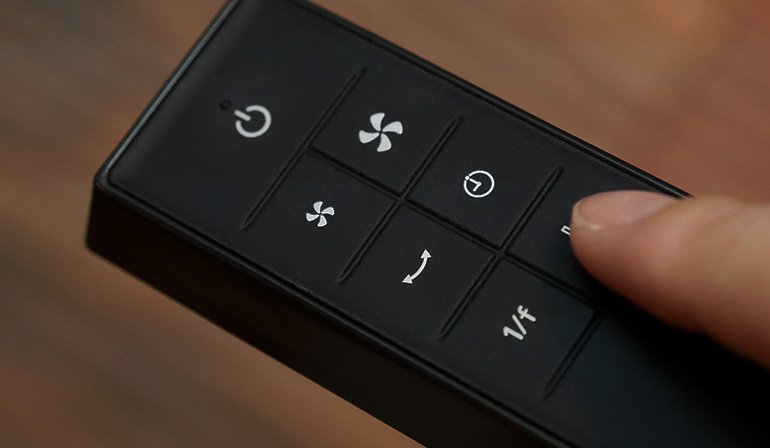 A hand pressing a button on a remote control, showing buttons for power, fan speed, and oscillation.