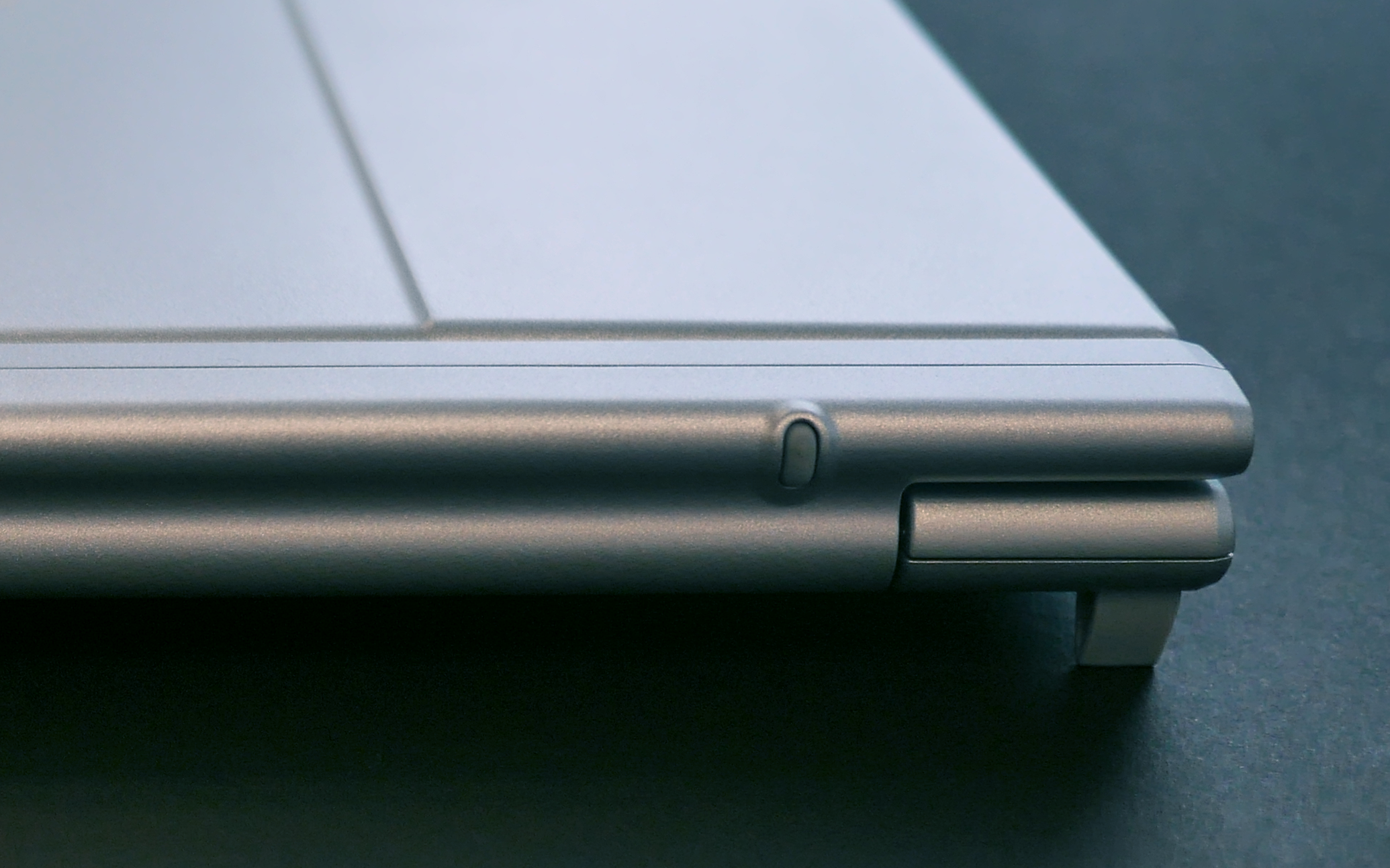 A close-up of the corner of a silver laptop with rounded edges, placed on a dark surface.