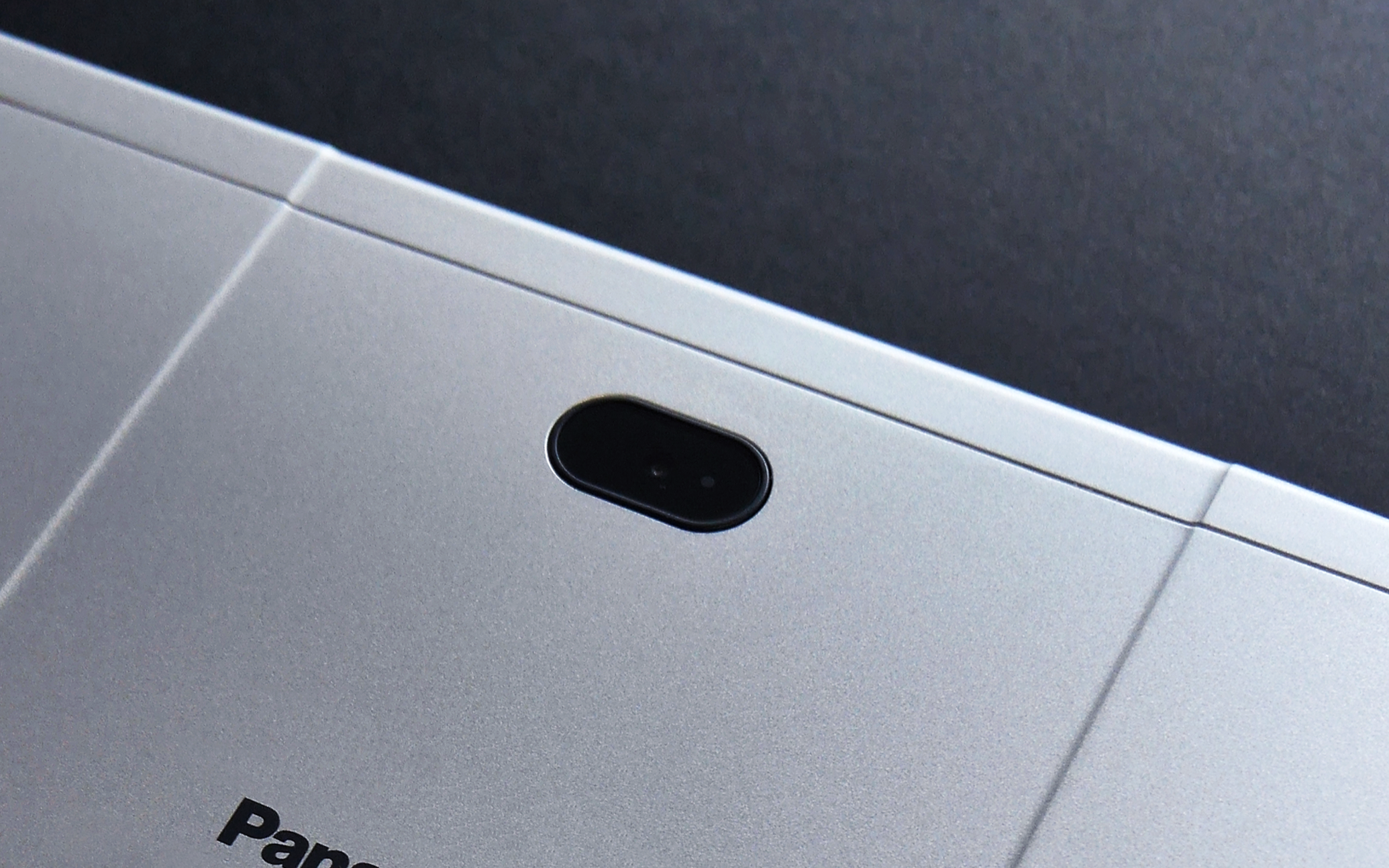 Close-up of the top edge of a silver laptop showing its camera and part of the brand logo.