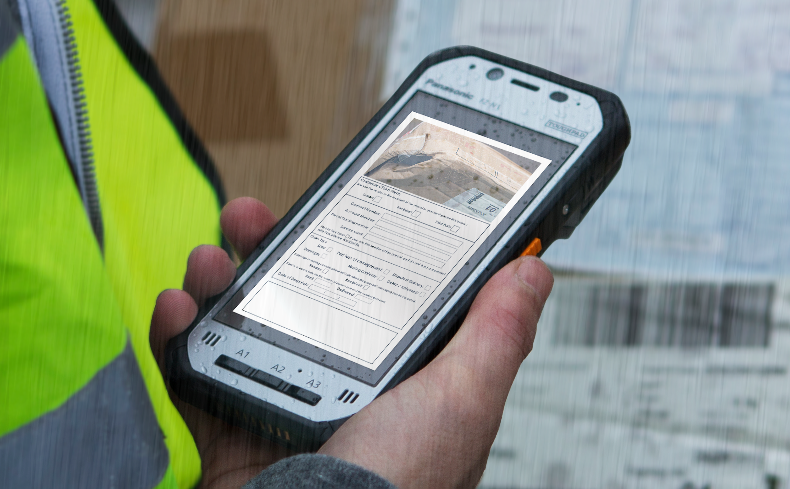 Toughpad screen held by a worker's right hand in the rain.