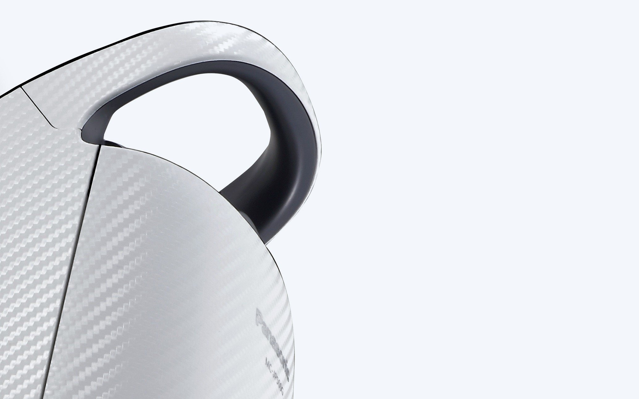 Close-up of a vacuum cleaner body showing a textured silver surface with a carbon fiber pattern and a black curved handle against a plain light background
