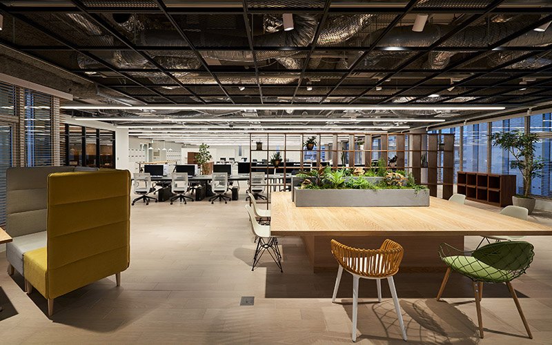 Spacious office with exposed ceiling, large wooden table with plants in center, various chairs and desks around