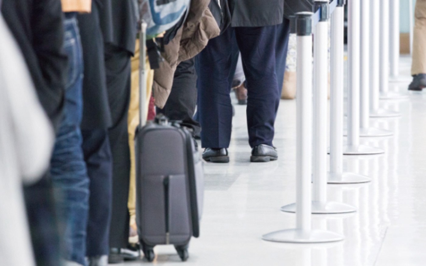 Line of travelers waiting for boarding at the airport, with suitcases, standing in front of guide signs