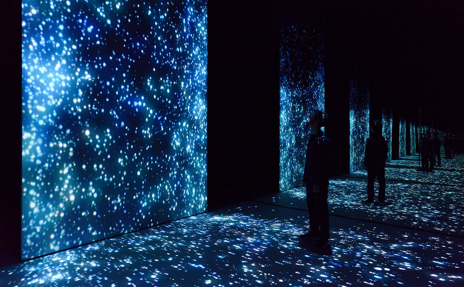 A space where a pale blue light shines in a dark space, and there are people watching it.