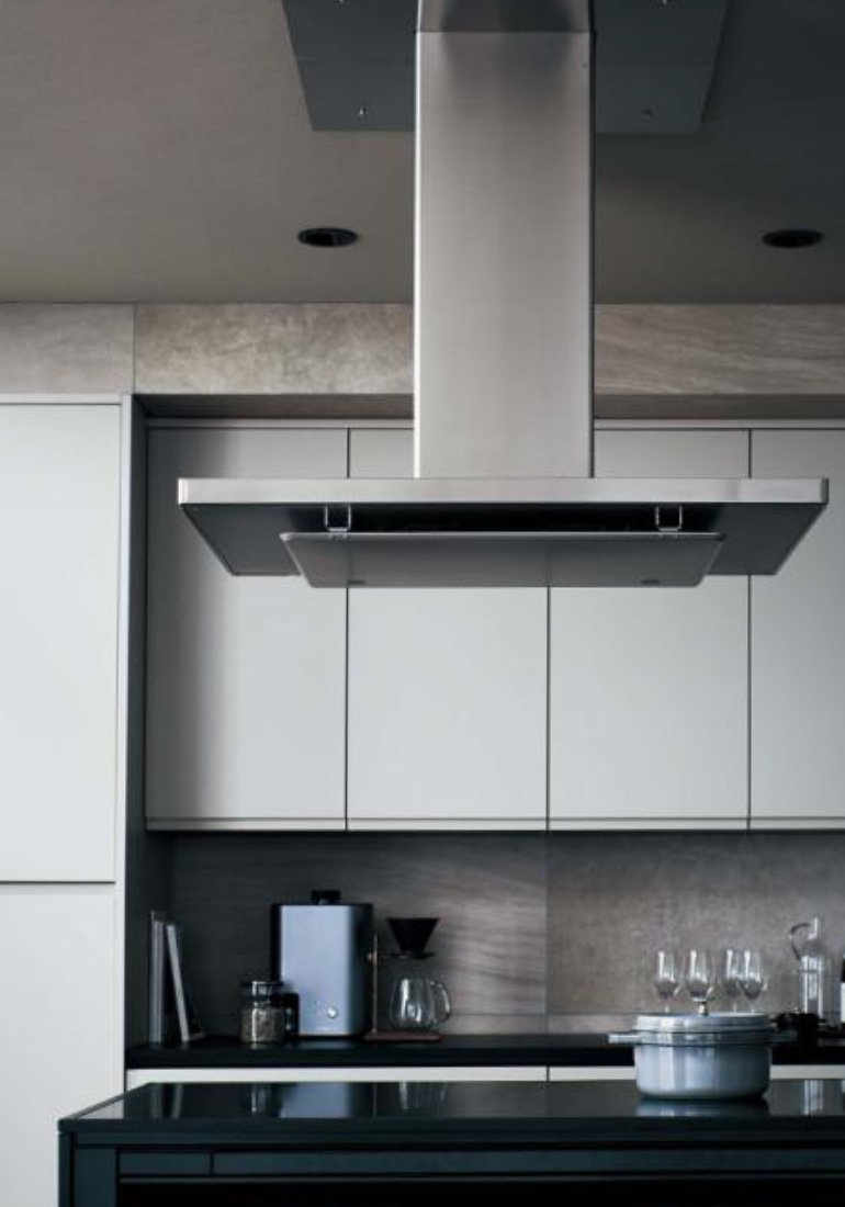 Modern kitchen with stainless steel range hood. White cabinets and black countertop, coffee maker with glass dripper, pot on the stove.