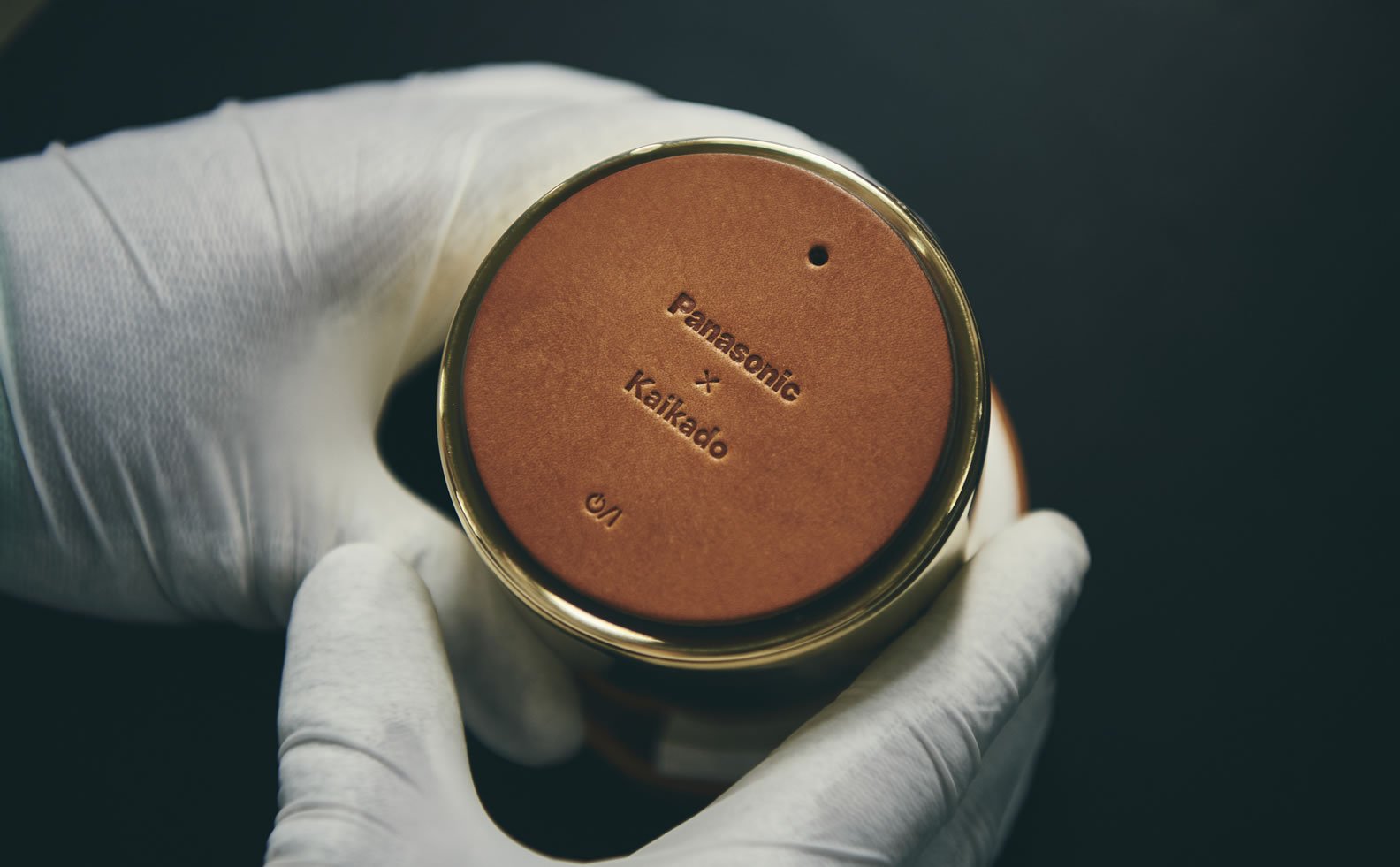 Bottom of a cylindrical speaker with gold rim and logo printed on the surface
