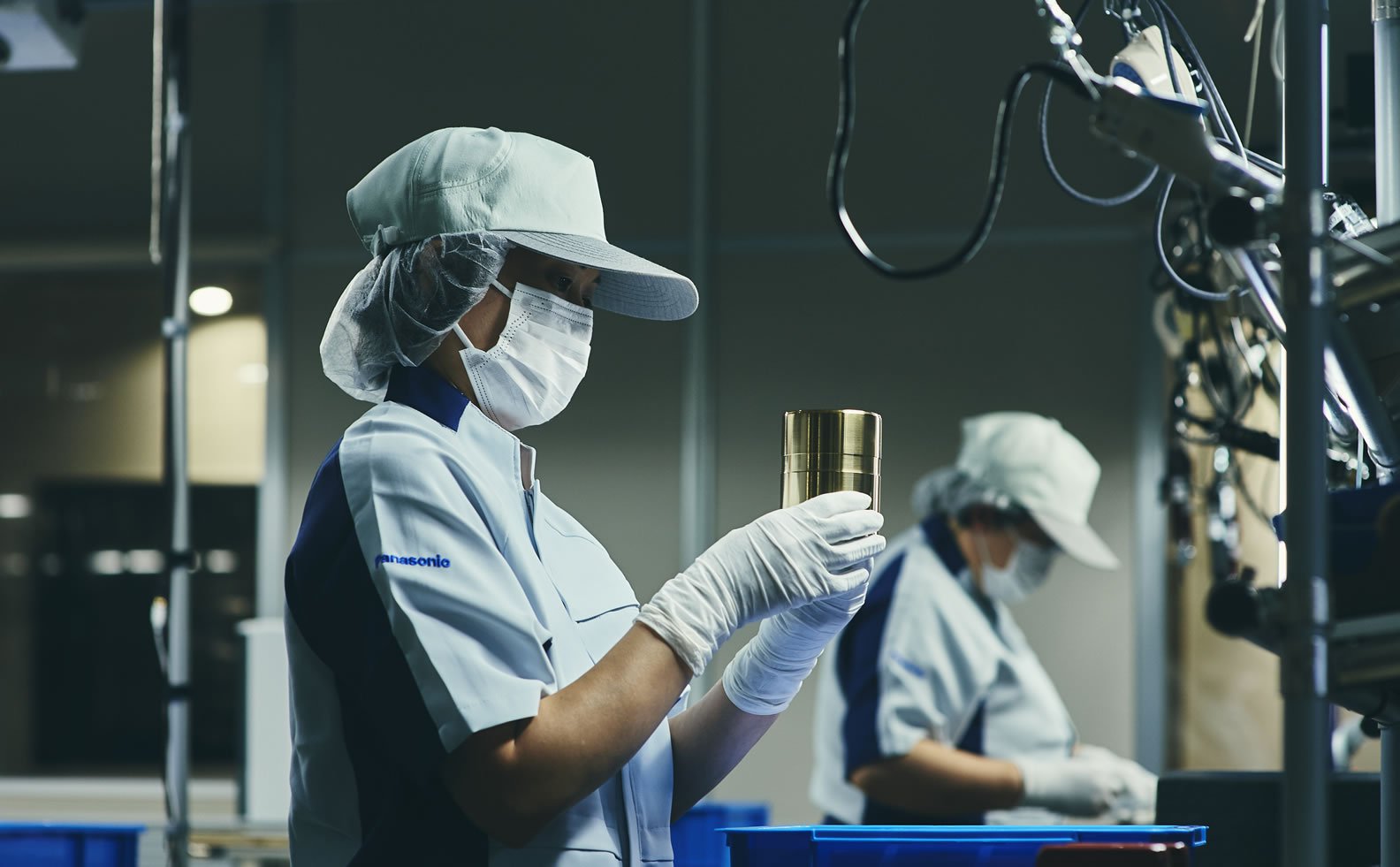 Factory inspector holding a metallic container, wearing a white coat and cap.