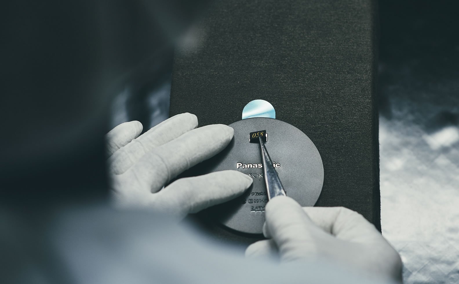 Person in gloves installing a serial number plate on a cylindrical speaker with a tool