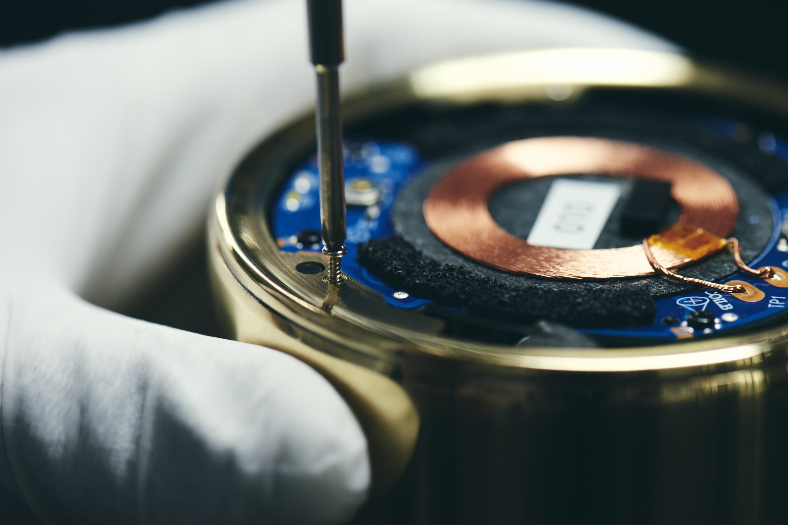 Inside of a cylindrical speaker with a tool securing a metal component, close-up view