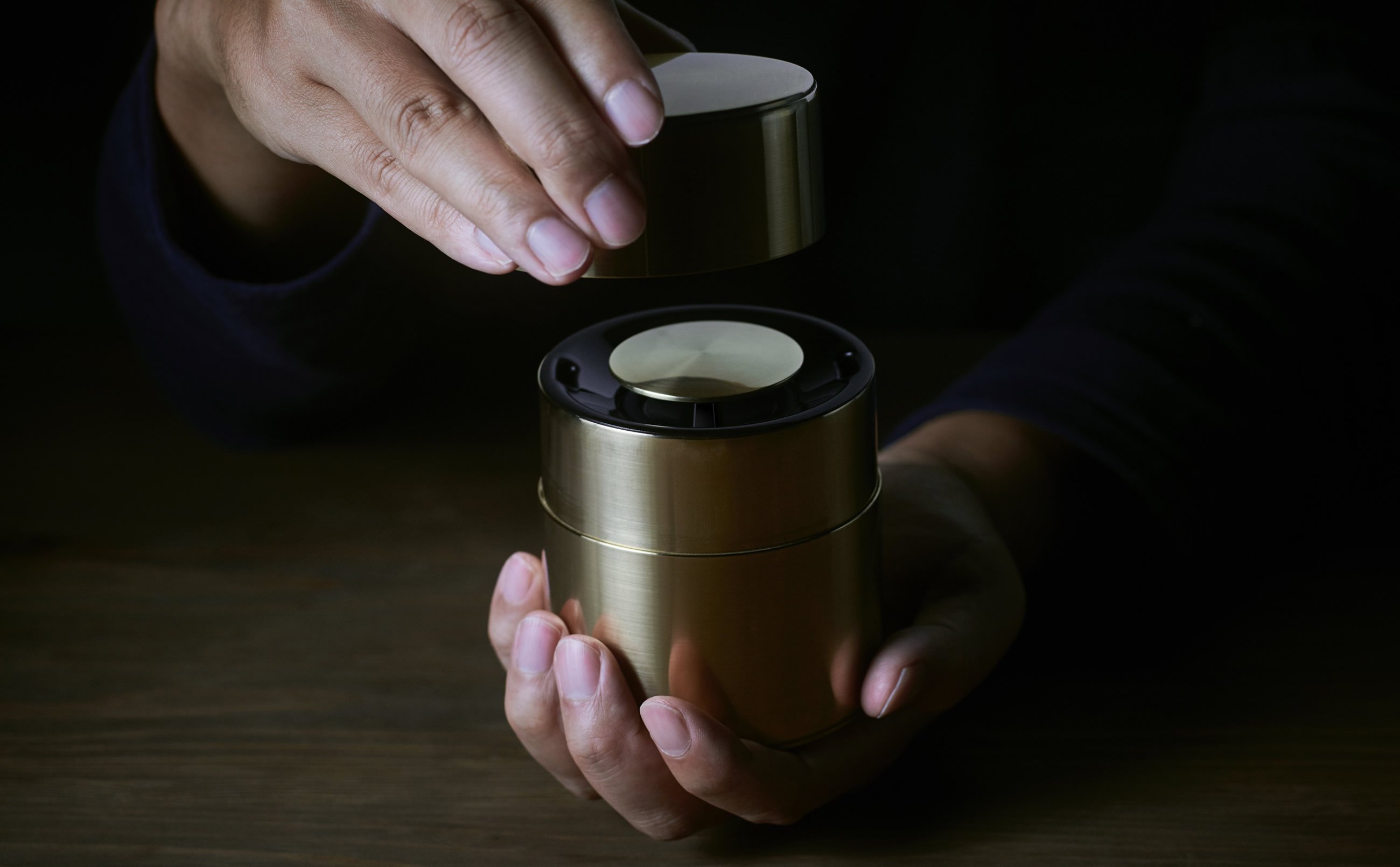 Hand holding open the lid of a tea canister speaker.