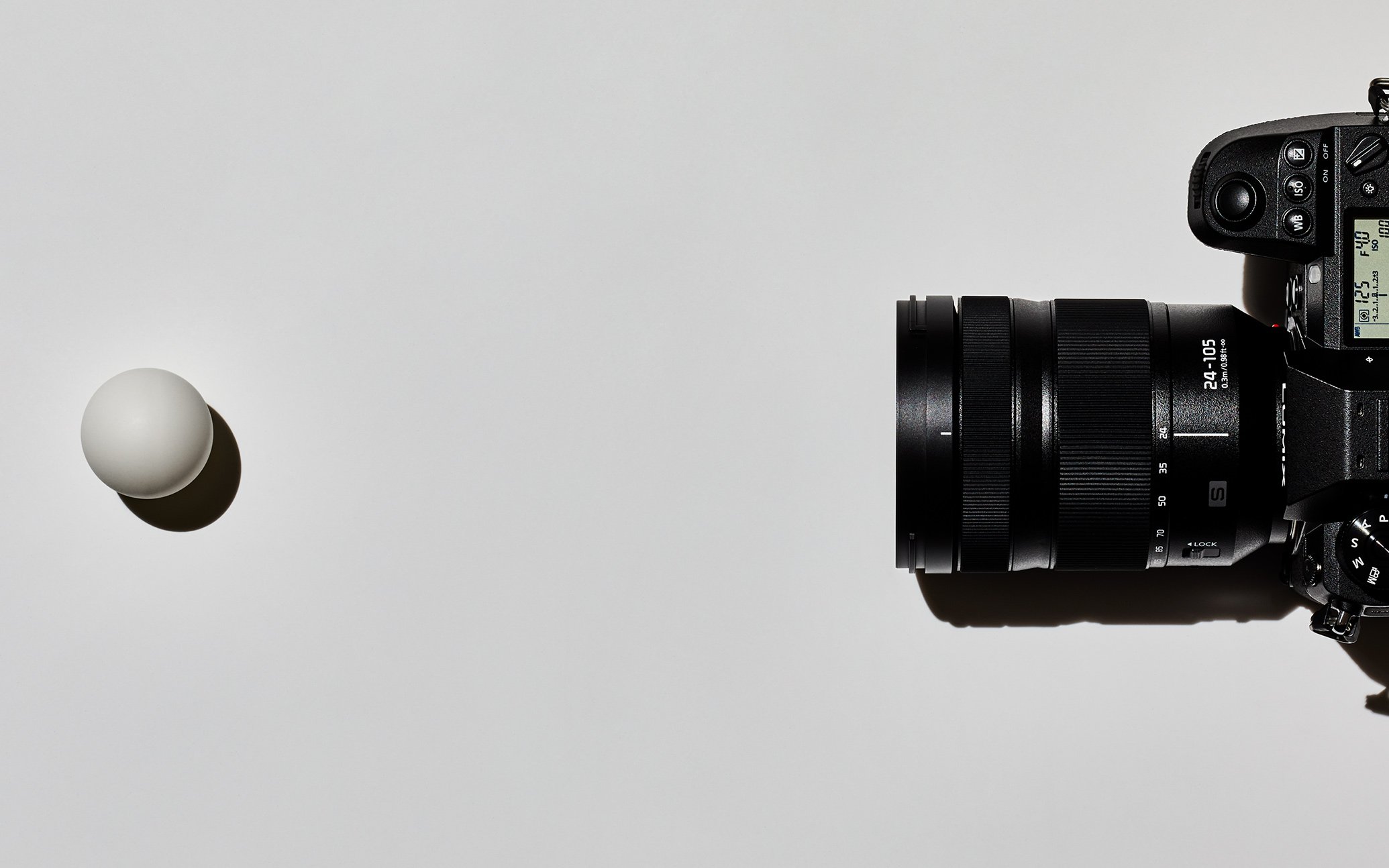 A camera and a white spherical object arranged in a minimalistic composition
