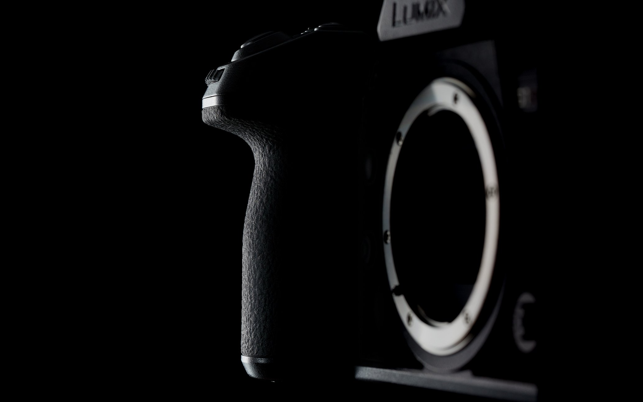 Black camera grip and lens mount ring highlighted on the Panasonic Lumix camera body against dark background