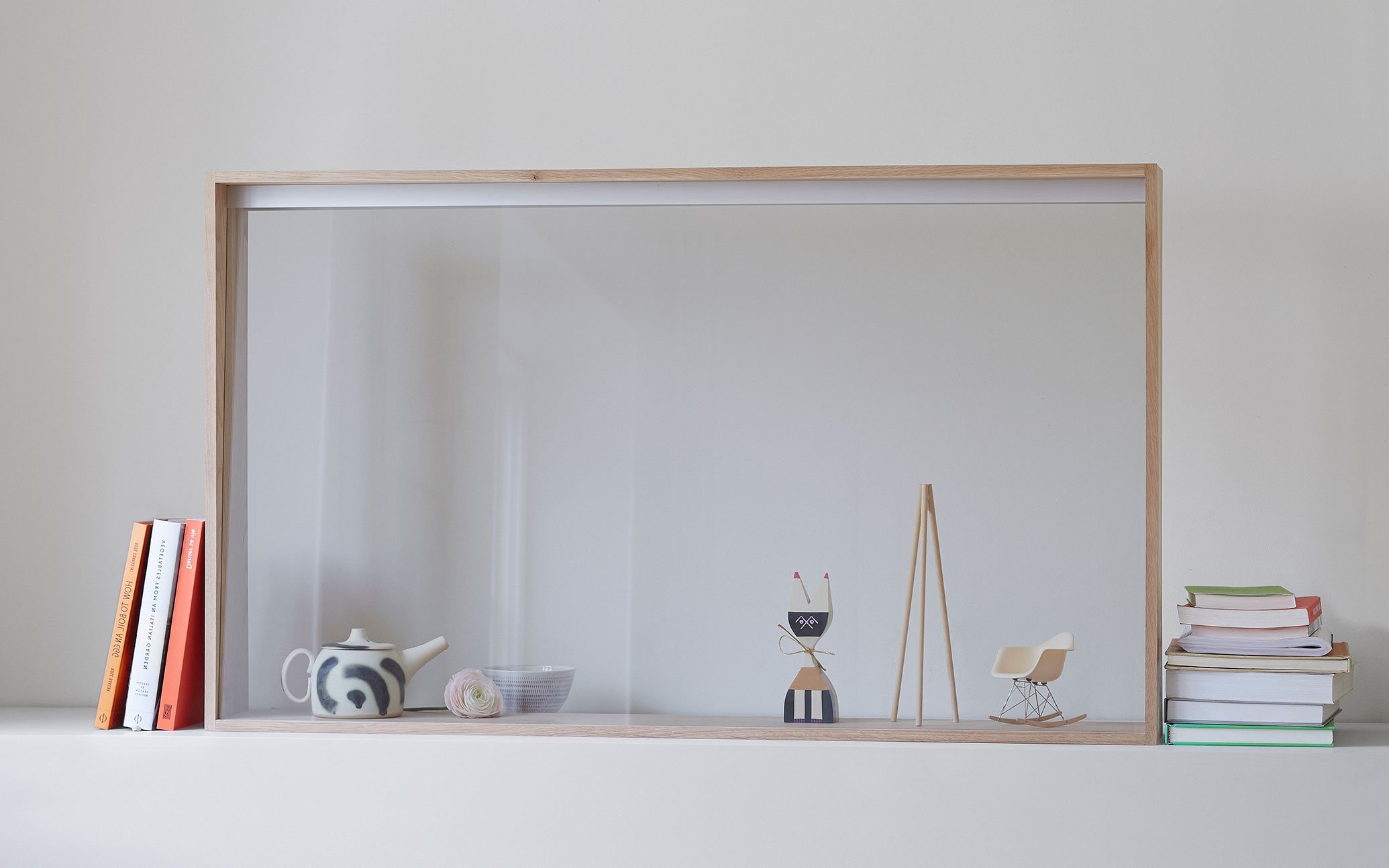 Books stacked behind wooden-framed transparent display, ceramic pot, wooden figurines, miniature chair, books arranged on both sides