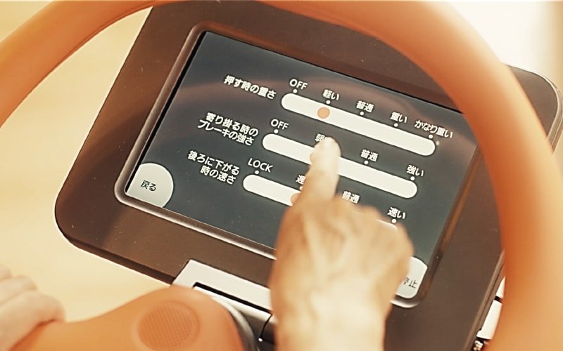 Settings interface on tablet screen. White slider bars and Japanese text on black background. Finger adjusting slider. Display with orange frame