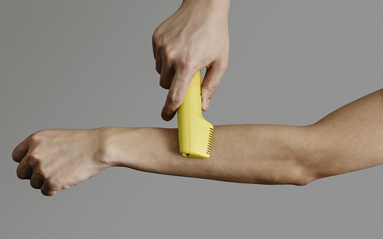 Close-up of a yellow electric shaver pressed against an arm, showing the device in use