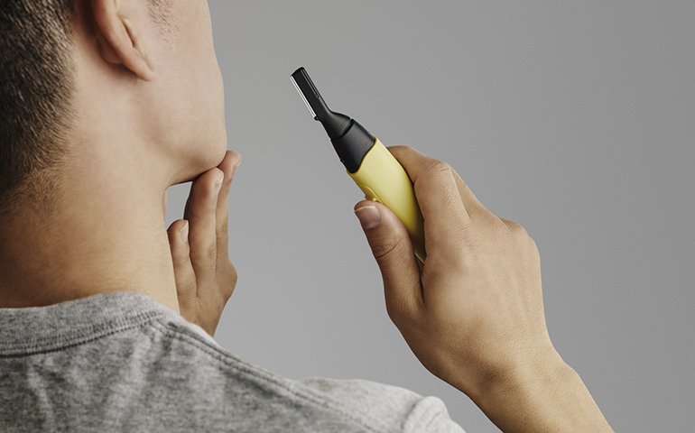 Man in a gray shirt holding a yellow nose hair trimmer near his nose