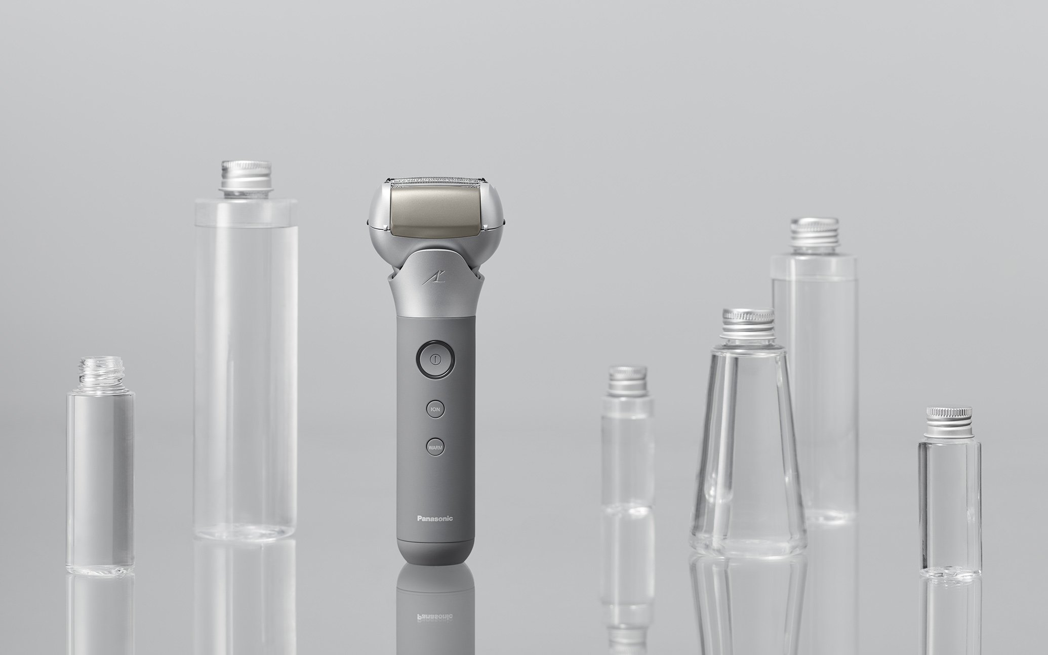 Front view of a gray electric shaver surrounded by clear containers, minimalistic style
