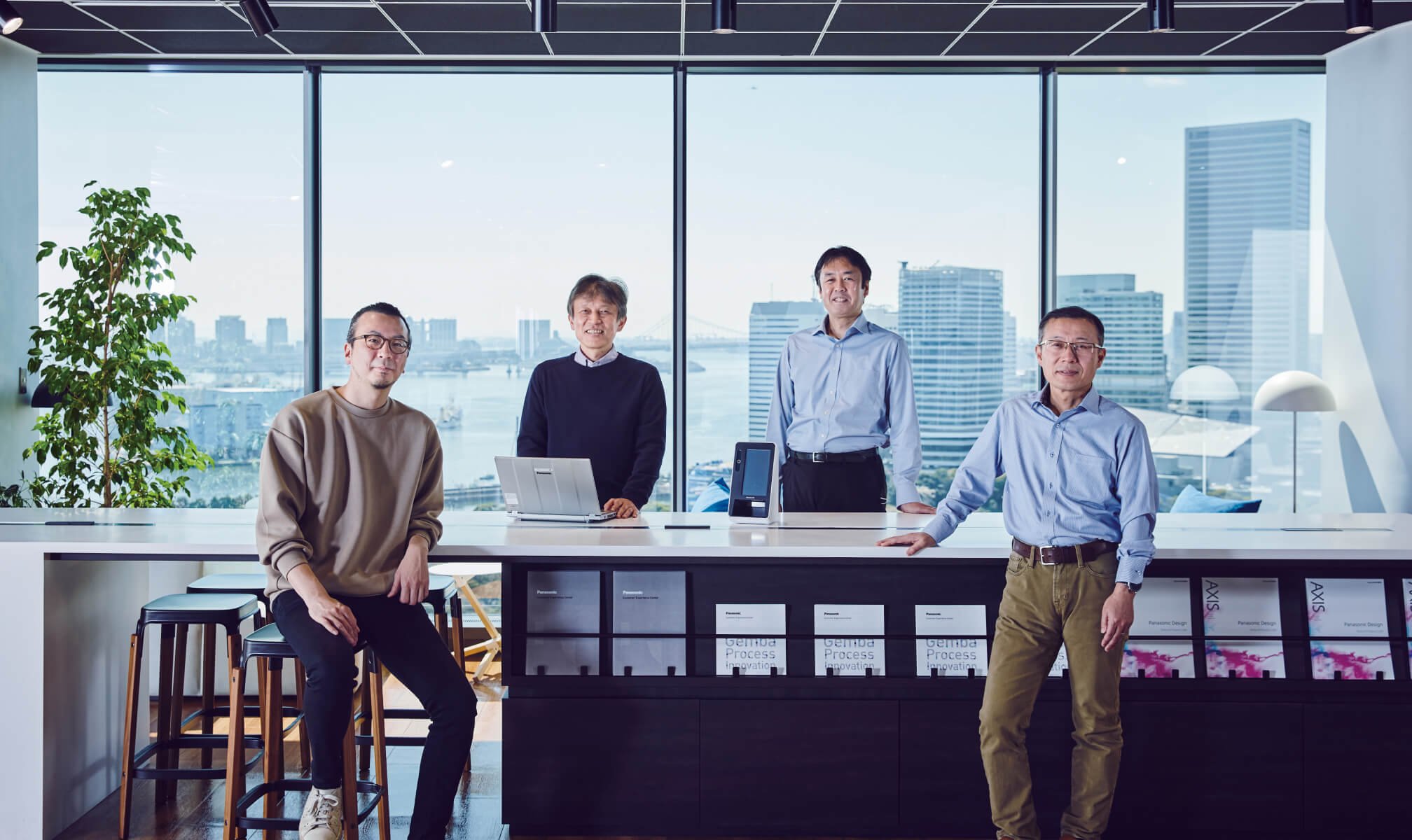 Four men standing at a counter in a conference room with large windows and city view