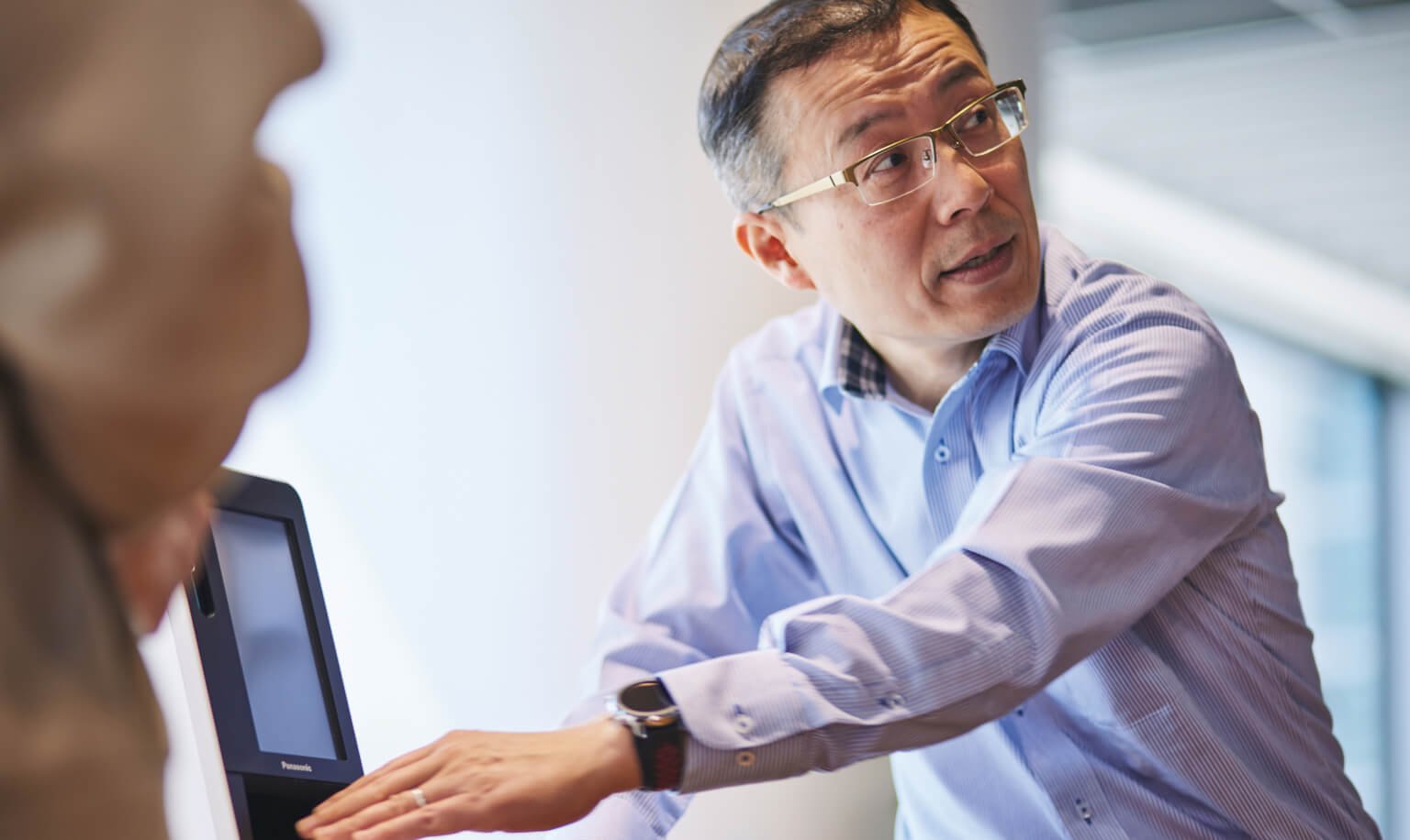 A man wearing a wristwatch in a conference room is operating a card reader and explaining how it works.