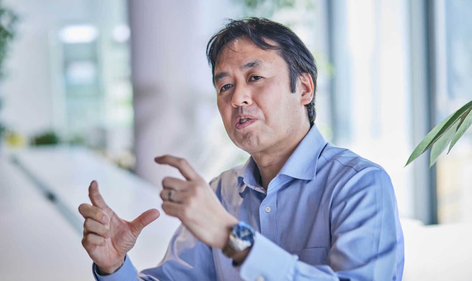 Man in blue shirt wearing wristwatch pointing at card reader on conference table