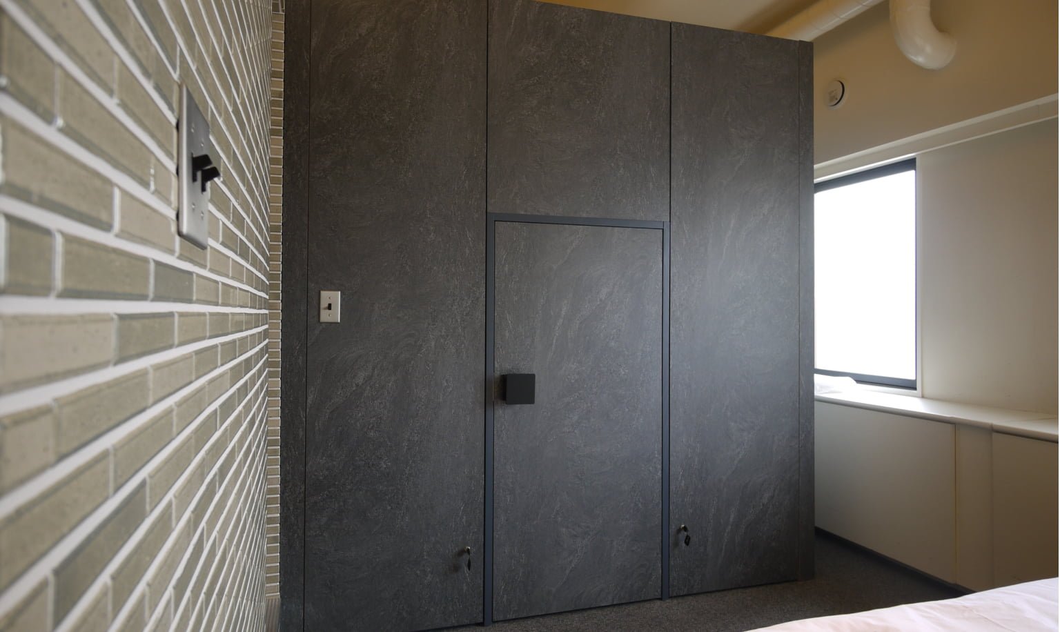 A room with a black wall-mounted door, wood-textured wall, large window, and white countertop