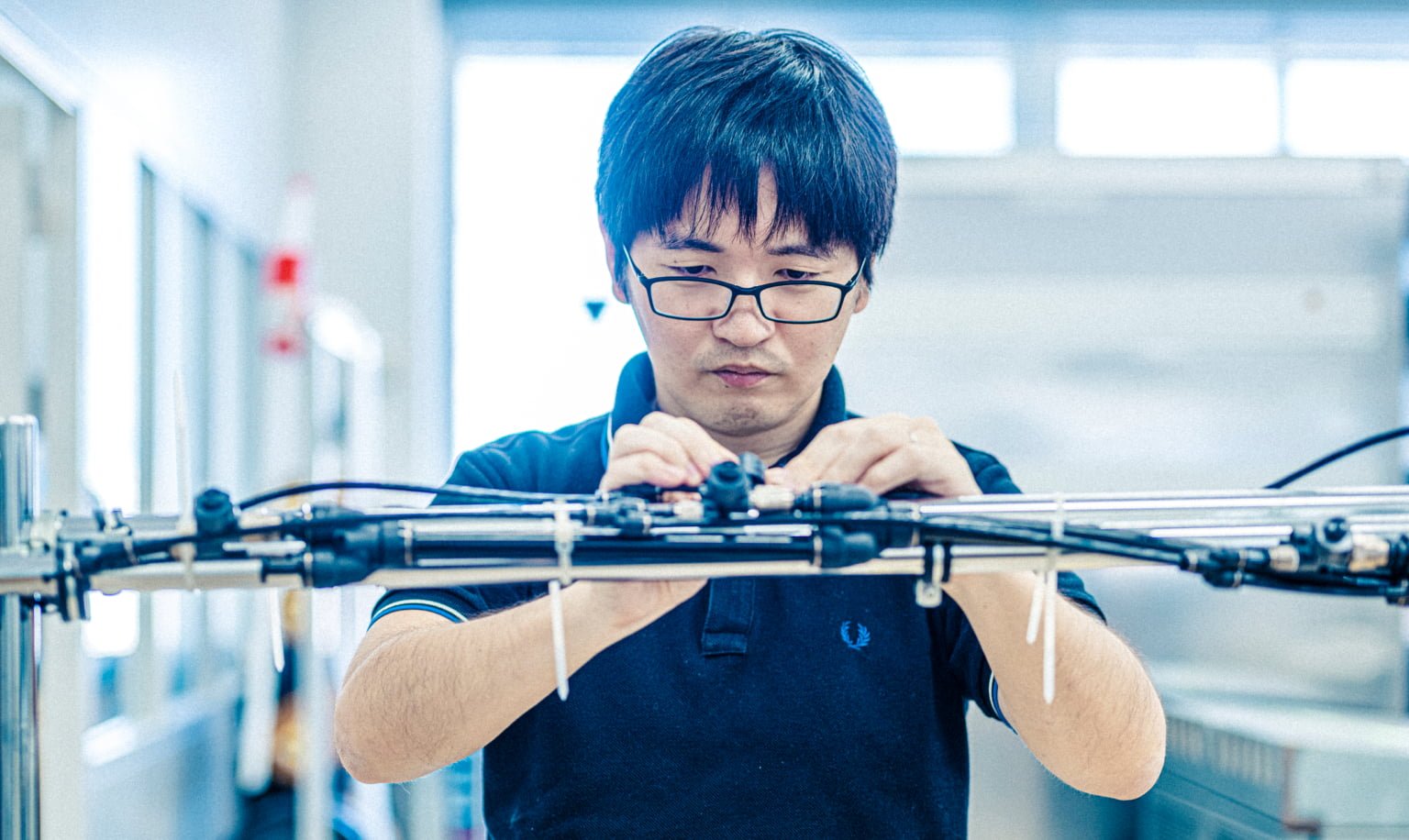Man with short hair wearing a black polo shirt working with tools in an indoor workshop