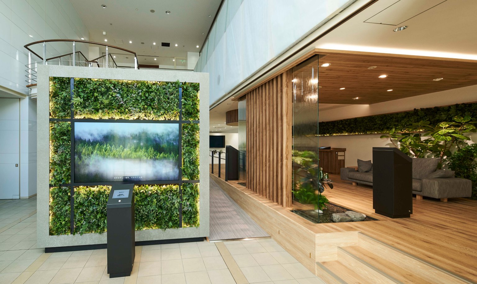 A lounge space featuring a green plant panel on the wall, a central display, a wooden partition, and sofas.