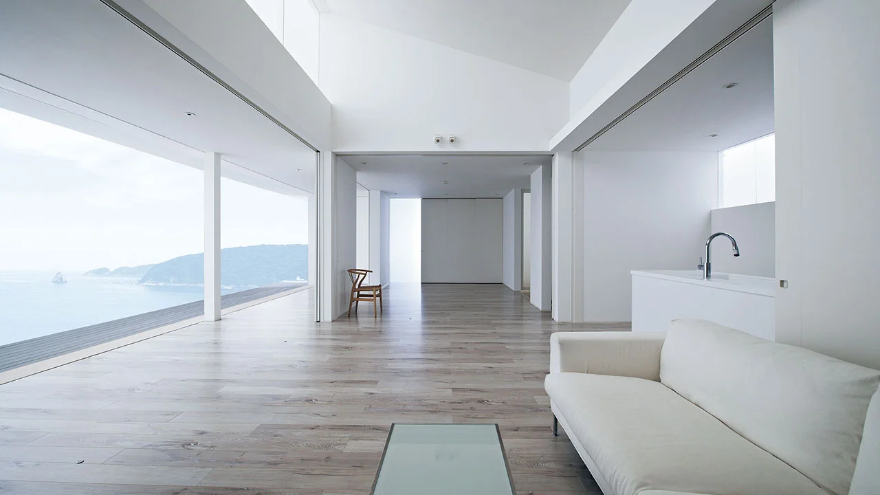 Interior of the building facing the sea, with white sofas and kitchen visible on the right.
