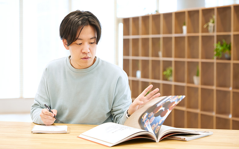 photo: Kotaro Iida sketches while looking at a magazine at a table