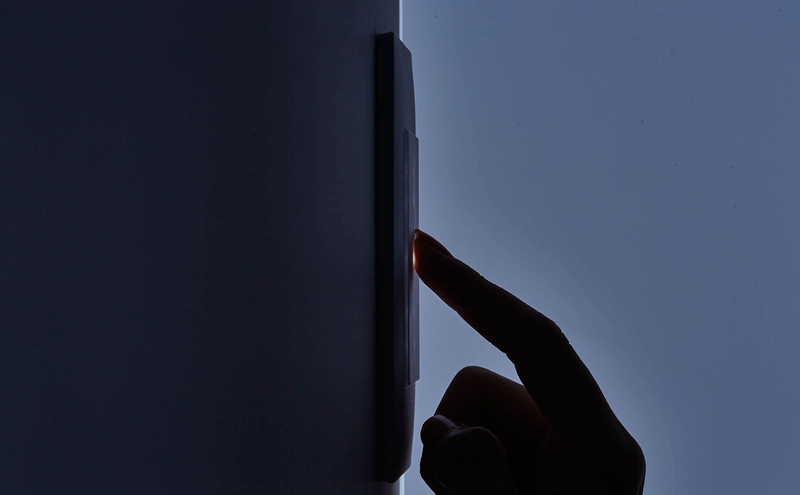 Index finger touching a switch on the wall in the dark.